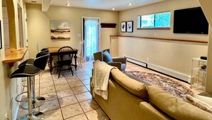 Ein Wohnzimmer mit einer Couch, Sesseln, einem Esstisch und einem an der Wand befestigten Fernseher.