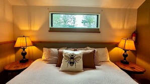 Ein Hotelzimmer mit einem Bett, zwei Nachttischlampen, einem Fenster mit Blick und einem bienenbezogenen Kopfkissen.