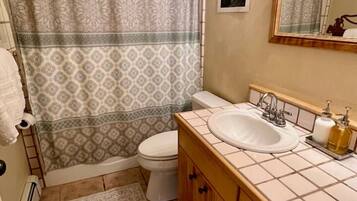 Une salle de bain avec un rideau de douche à motifs, des toilettes, un lavabo avec un miroir et des meubles en bois.
