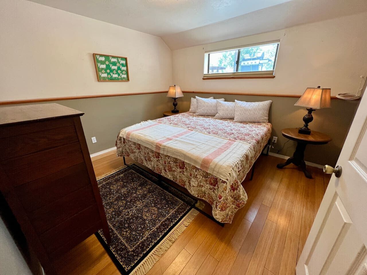 A bedroom with a bed, a nightstand, a dresser, a window, and a door.