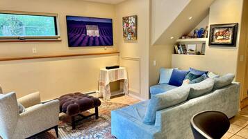 Un salon comprenant un canapé, un fauteuil, un pouf et un téléviseur fixé au mur.