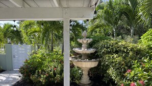 A garden with a stone fountain, lush greenery, and a white gate.