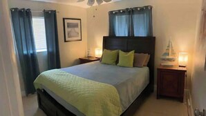 A bedroom with a bed, two bedside tables, a nightstand, a ceiling fan, and a window with curtains.