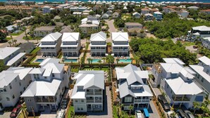 Zona residencial a la costa amb diverses cases de planta baixa i pis, amb porxades i una piscina central.