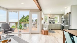 A modern kitchen with a large island, a dining area with a table and chairs, and a view of the outdoors. - Sunset Cove by Avantstay Beachfront w/ Balcony! (Arch Cape)