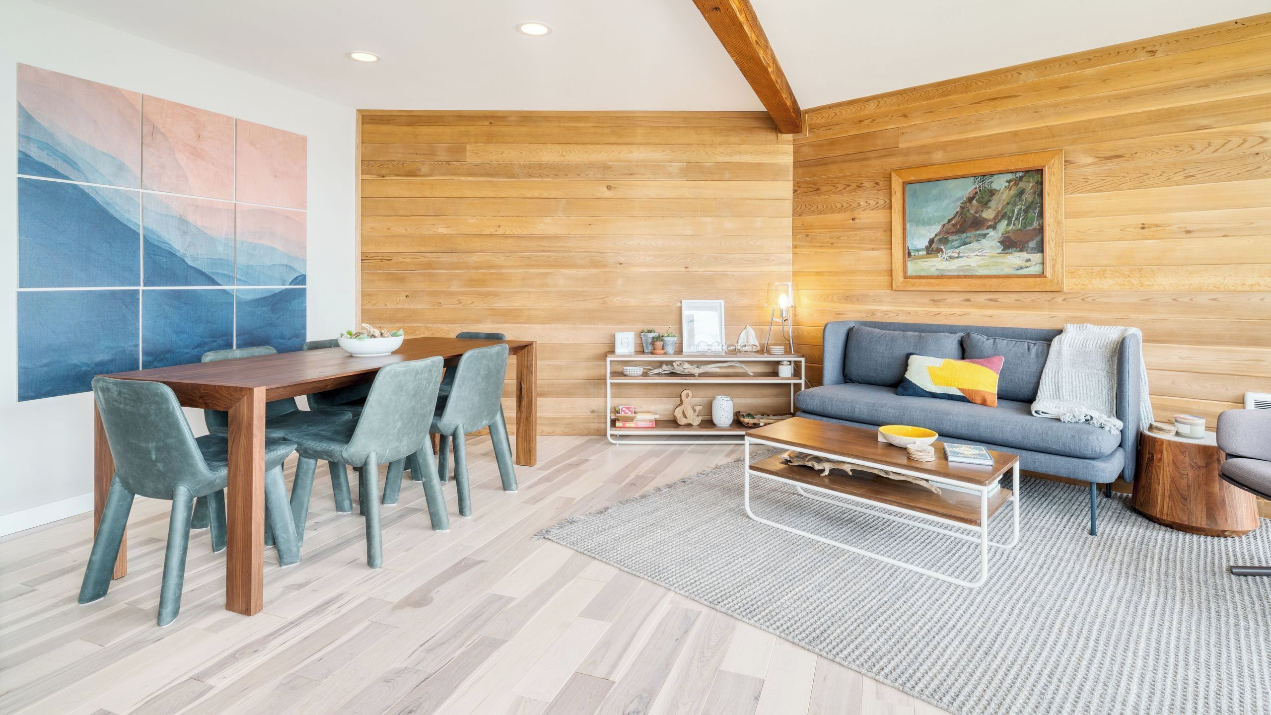 Un salon moderne avec un mur en bois, un coin repas avec une table et des chaises en bois, un canapé avec des coussins et un tableau accroché au mur.