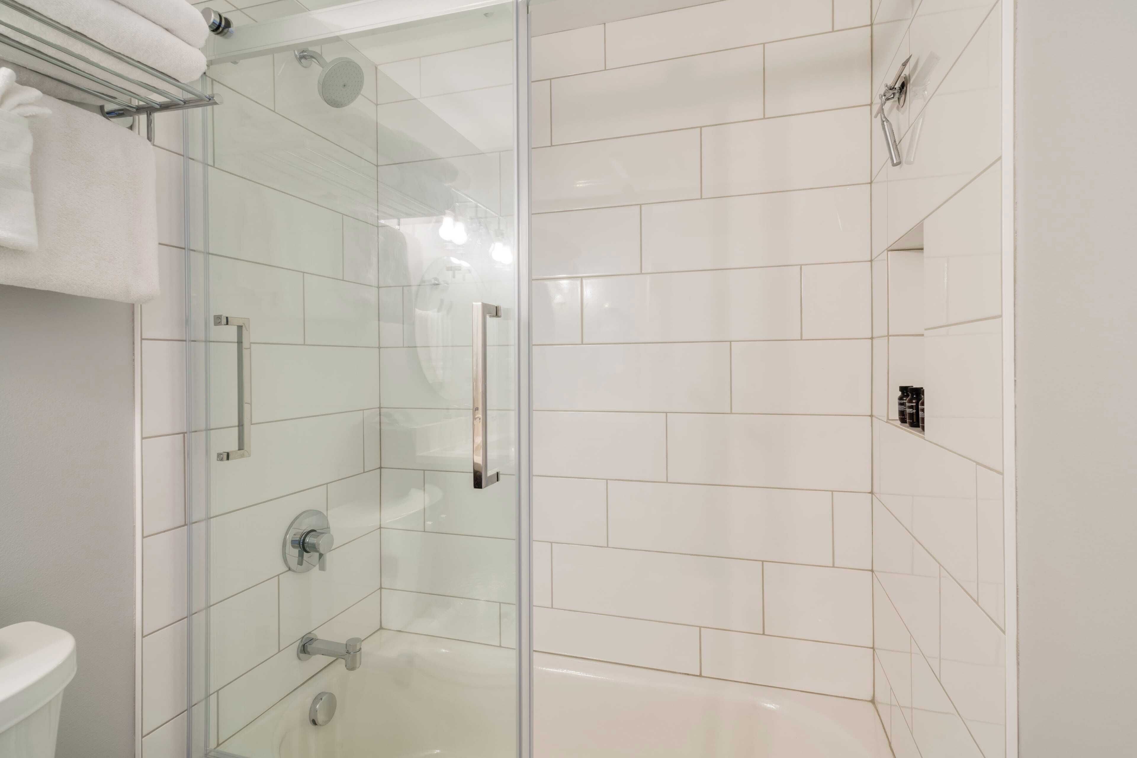 A modern bathroom with a glass-enclosed shower, white tiles, and a visible toilet.