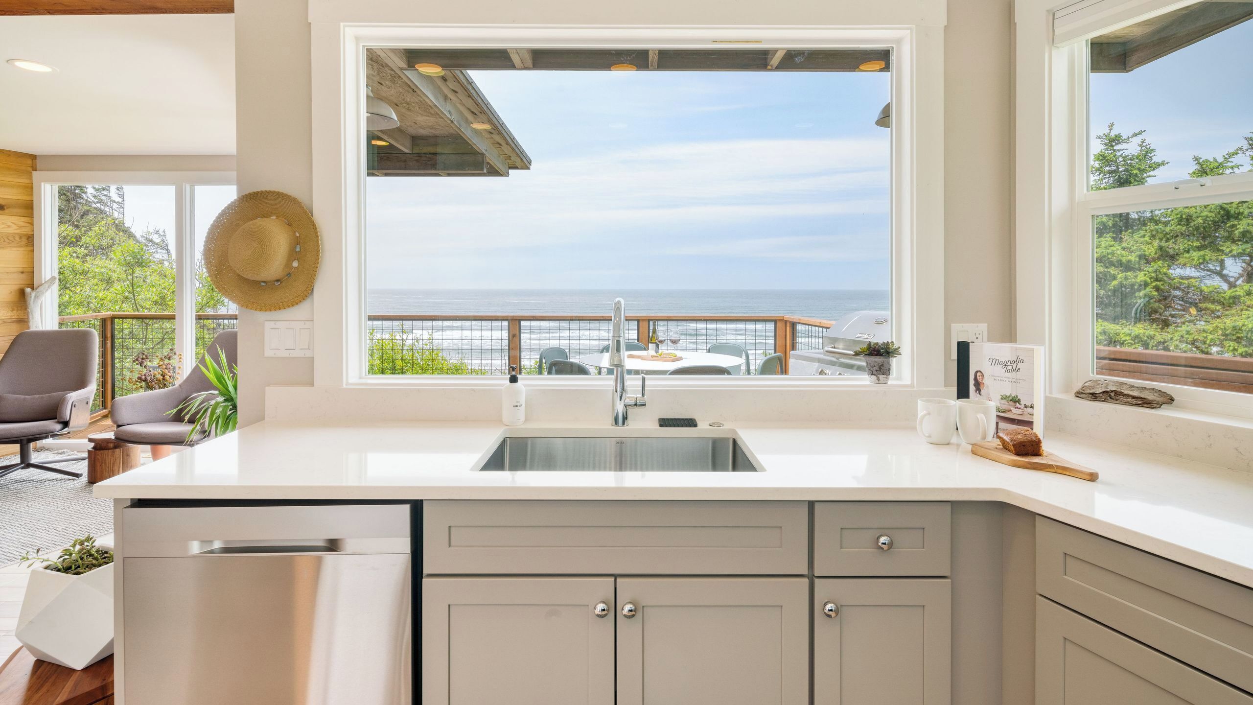 A modern kitchen with a large window overlooking a scenic ocean view, a built-in dishwasher, and a rustic wooden ceiling.