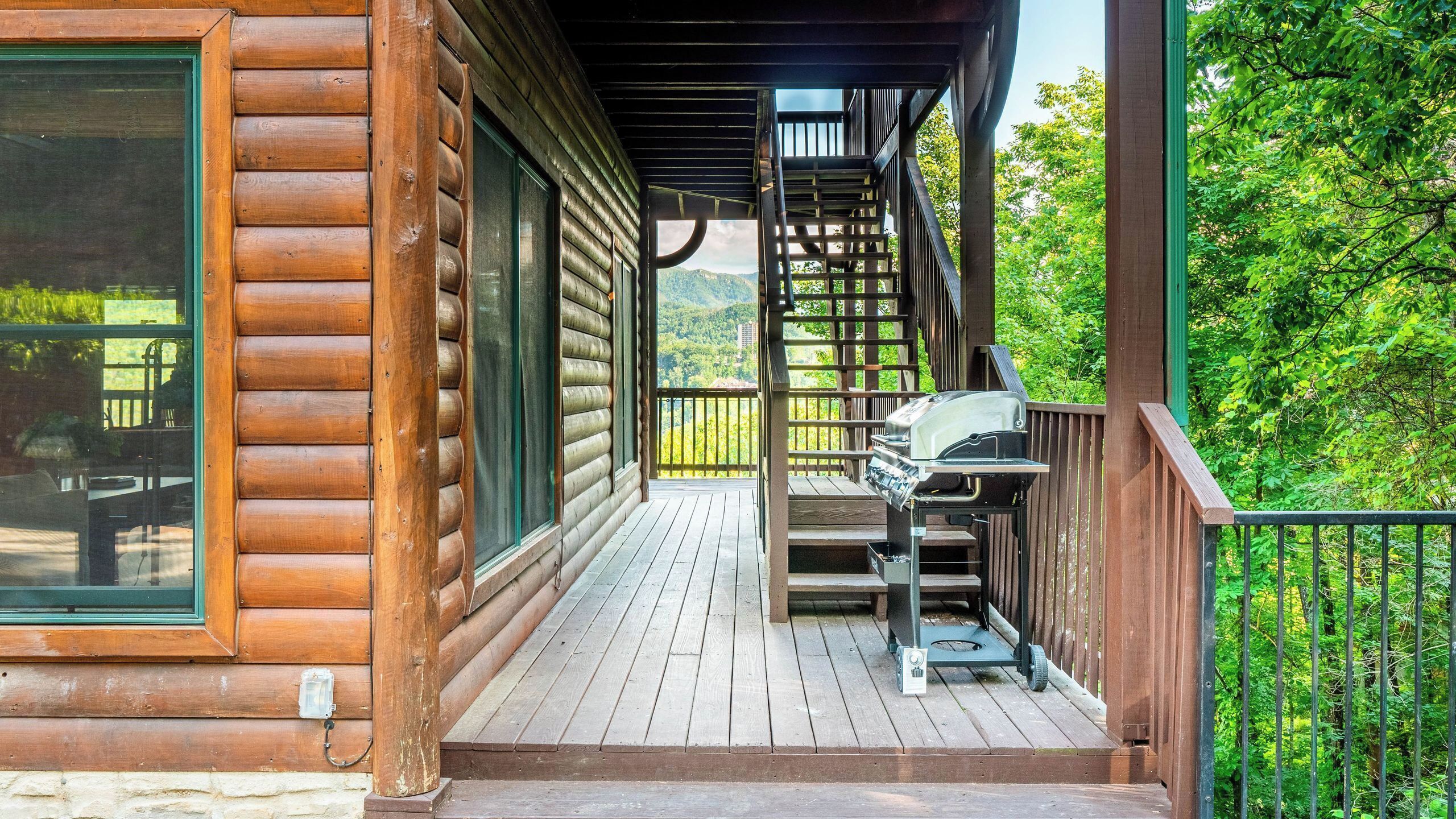 Une cabane en bois dotée d’une terrasse, d’un barbecue et offrant une vue sur une zone boisée.