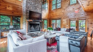 A spacious living room with a stone fireplace, large windows, and a cozy seating area.