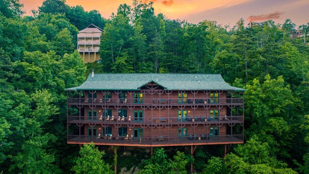 A multi-story wooden building with balconies, surrounded by dense forest. - Hickory Ridge by Avantstay Sleeps 20! Incredible Private Elevated Cabin (Gatlinburg)