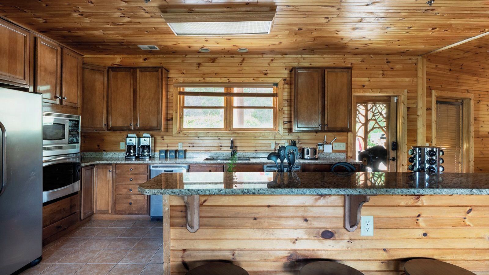 Een houten keukentje in een chalet, met een centraal eiland, ingebouwde apparaten en een groot raam.