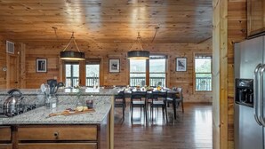 A wooden cabin interior with a kitchen, dining area, and a refrigerator. - Hickory Ridge by Avantstay Sleeps 20! Incredible Private Elevated Cabin (Gatlinburg)