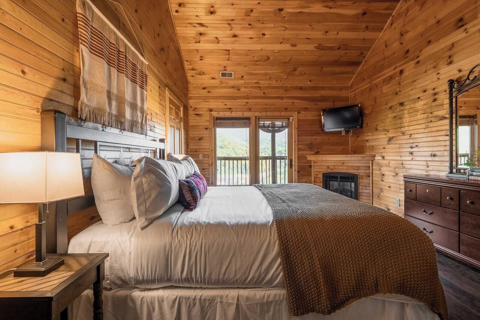 Acogedor dormitorio de cabaña de madera con cama, cómoda, televisor y chimenea.