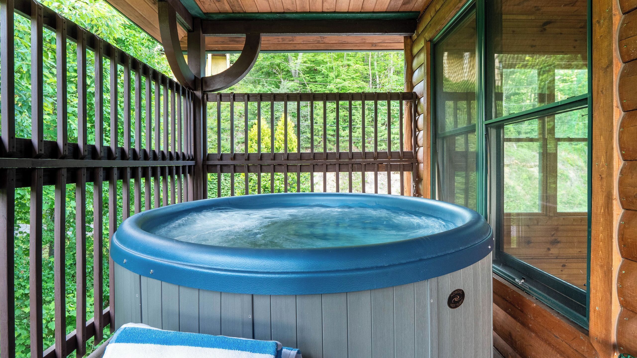 A hot tub in a wooden cabin with a wooden deck and a window.