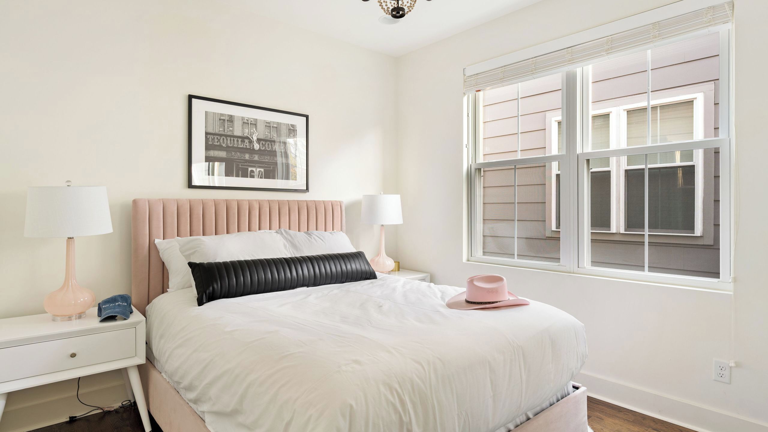 Une chambre à coucher avec un lit, deux tables de chevet, une fenêtre et un tableau encadré au mur.