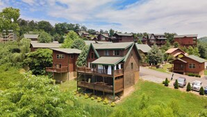 A lodge with a prominent wooden structure, a covered porch, and a view of surrounding buildings and greenery. - Tennessee Blue by Avantstayheart of Pigeon Forge! (Pigeon Forge)