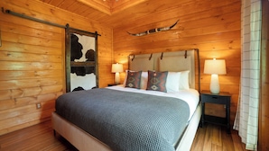 A wooden-paneled bedroom with a bed, two bedside lamps, and a headboard. - Tennessee Blue by Avantstayheart of Pigeon Forge! (Pigeon Forge)