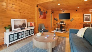 A cozy cabin-style room with a wooden interior, a television mounted on the wall, a dining table with chairs, and a blue sofa. - Tennessee Blue by Avantstayheart of Pigeon Forge! (Pigeon Forge)