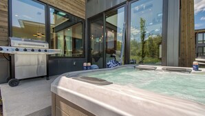 A hot tub with a wooden deck, a barbecue grill, and a glass-enclosed room with large windows. - Encore by Avantstayminutes From the Slopes in PC! w/ Hot Tub (Park City)