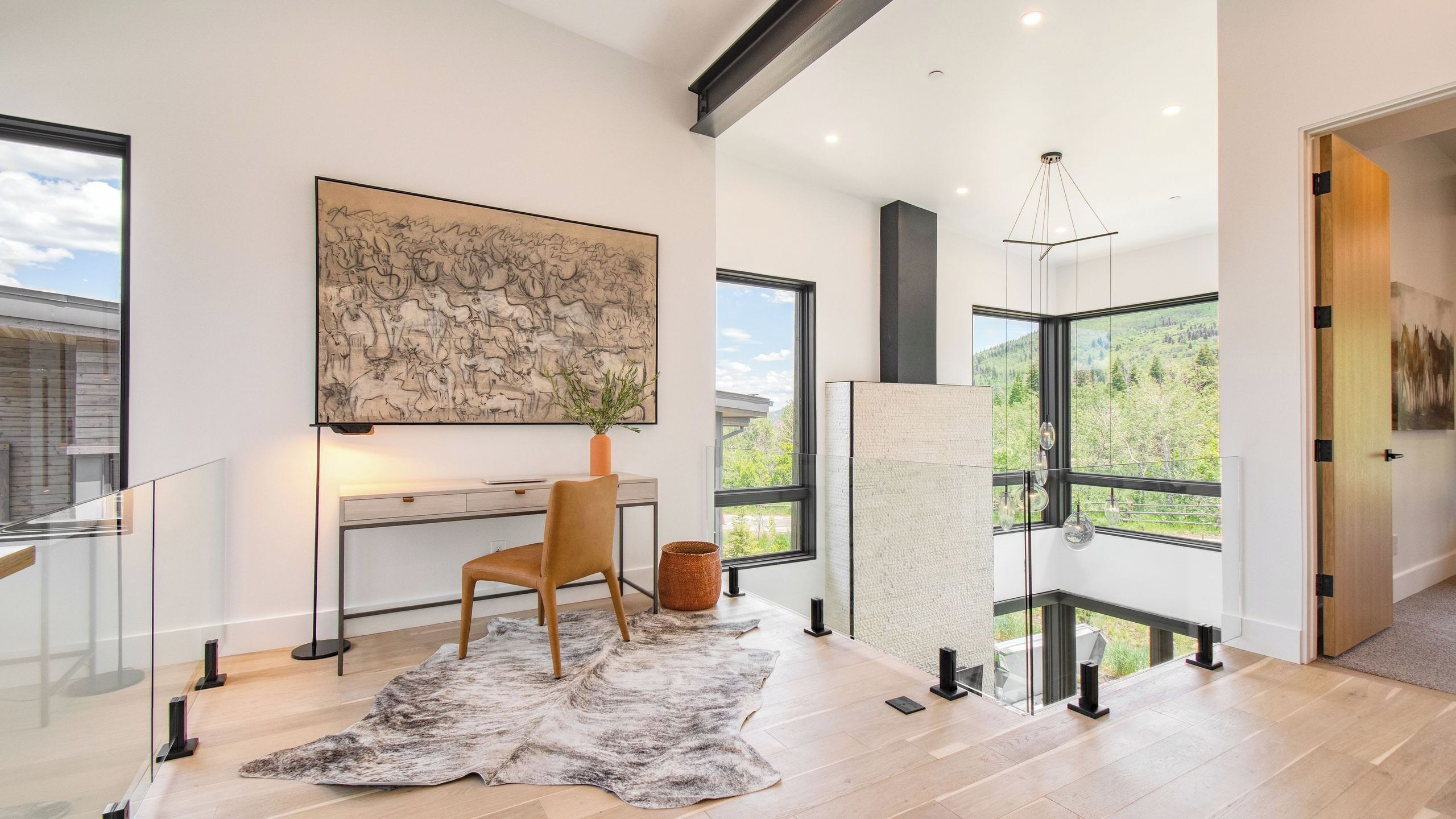 Una habitación moderna con escritorio, silla, ventanas amplias y una lámpara colgante.