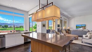 A modern kitchen with a large island, a dining area with a sofa, and a view of a golf course.