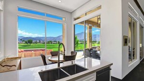 A modern kitchen with large windows offering a view of a golf course and mountains.