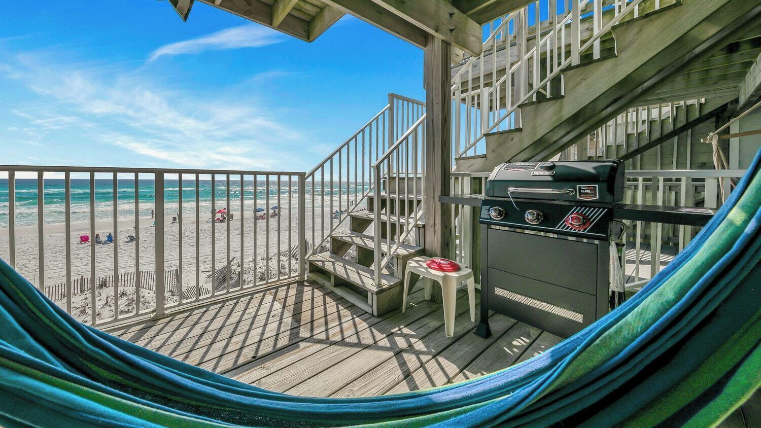 A beachside balcony with a hammock, a grill, and a view of the beach.