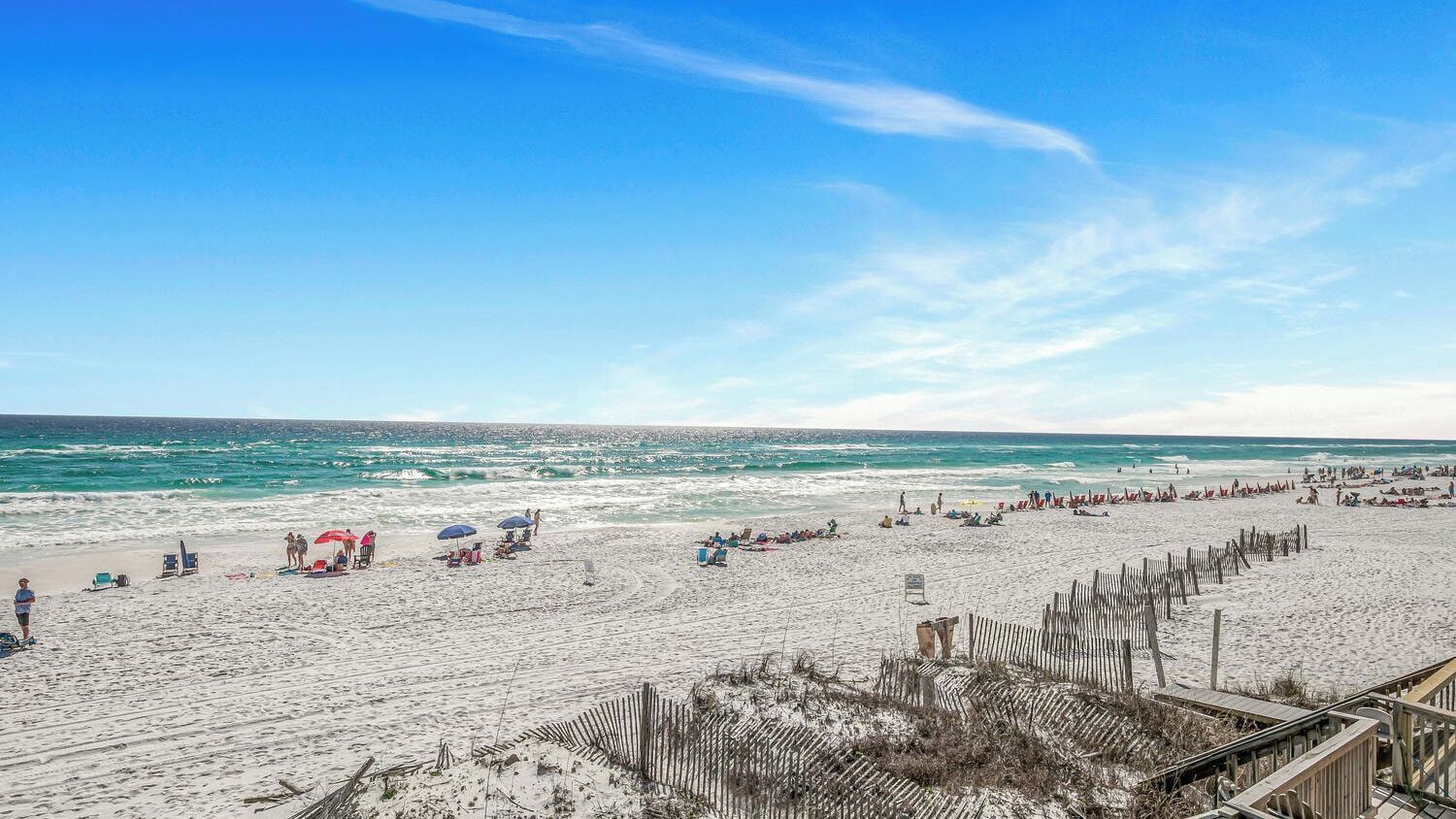 A beach with people and umbrellas, a wooden fence, and a clear sky.
