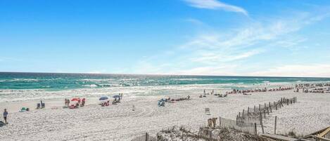 A beach with people and umbrellas, a wooden fence, and a clear sky.
