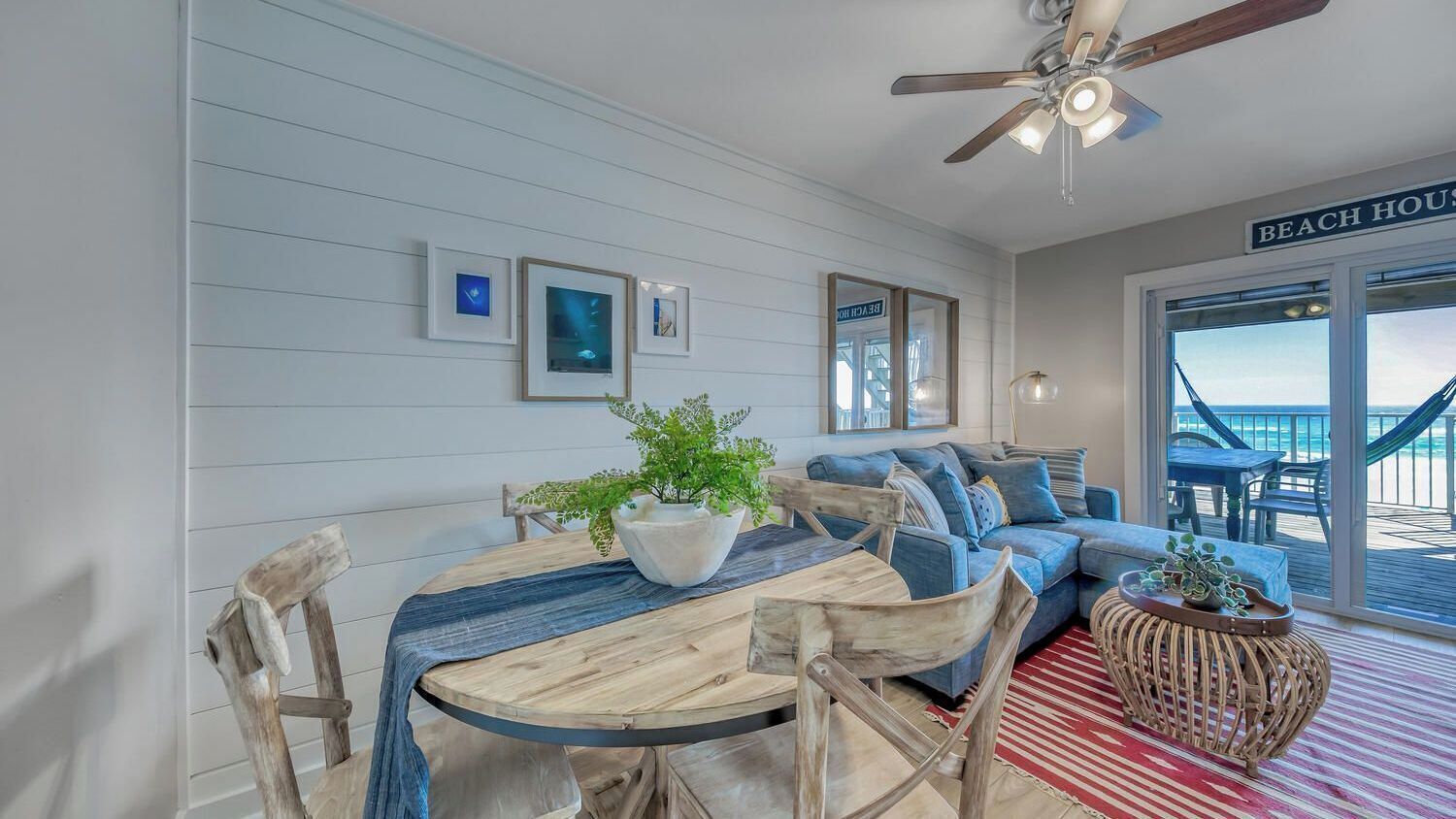 A beach house interior with a dining area, a sofa, and a view to the beach.