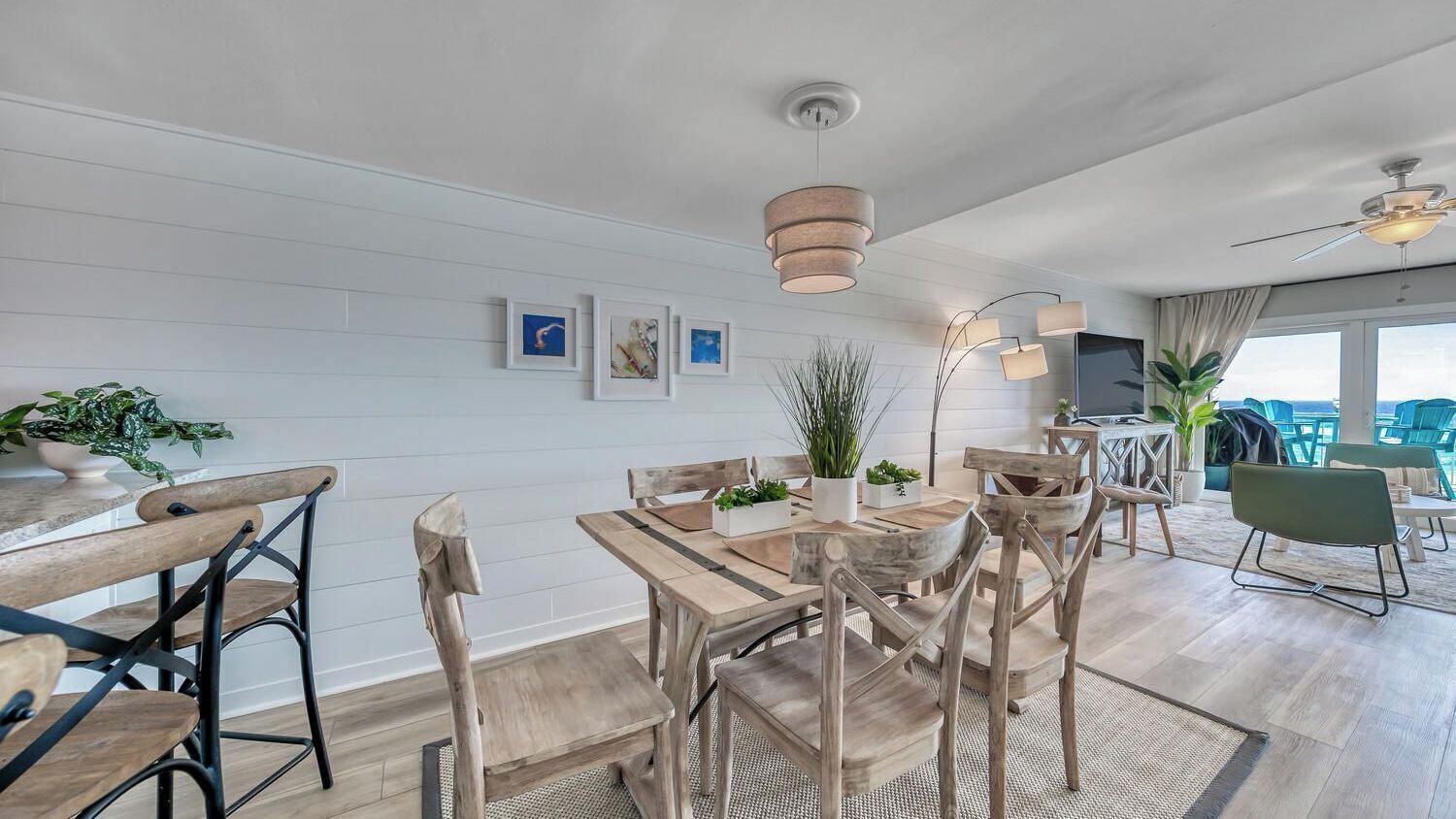 Un espace repas avec des meubles en bois, des luminaires suspendus et des œuvres d’art encadrées accrochées au mur.