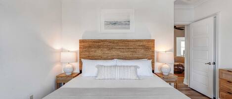 A bedroom with a large bed, two bedside lamps, a wooden headboard, and a framed picture on the wall.