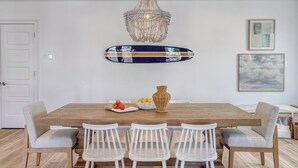 Ein Essbereich mit Holztisch, weißen Stühlen, einer Chandelier und Wandbildern.