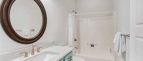 Une salle de bain avec un grand miroir, un lavabo à deux robinets, des toilettes et un espace douche.