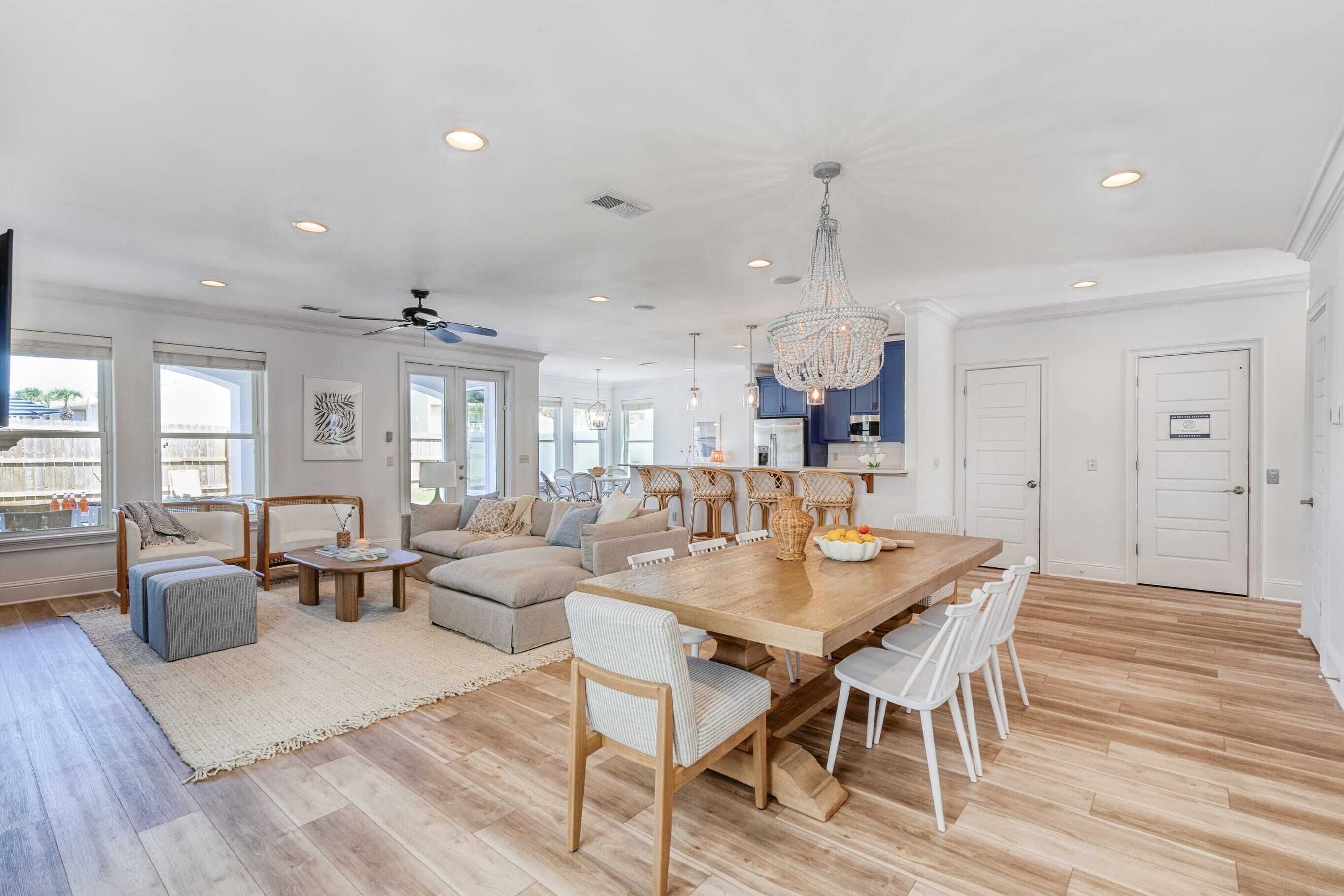 A spacious living room with a large wooden dining table, comfortable seating, and a chandelier.