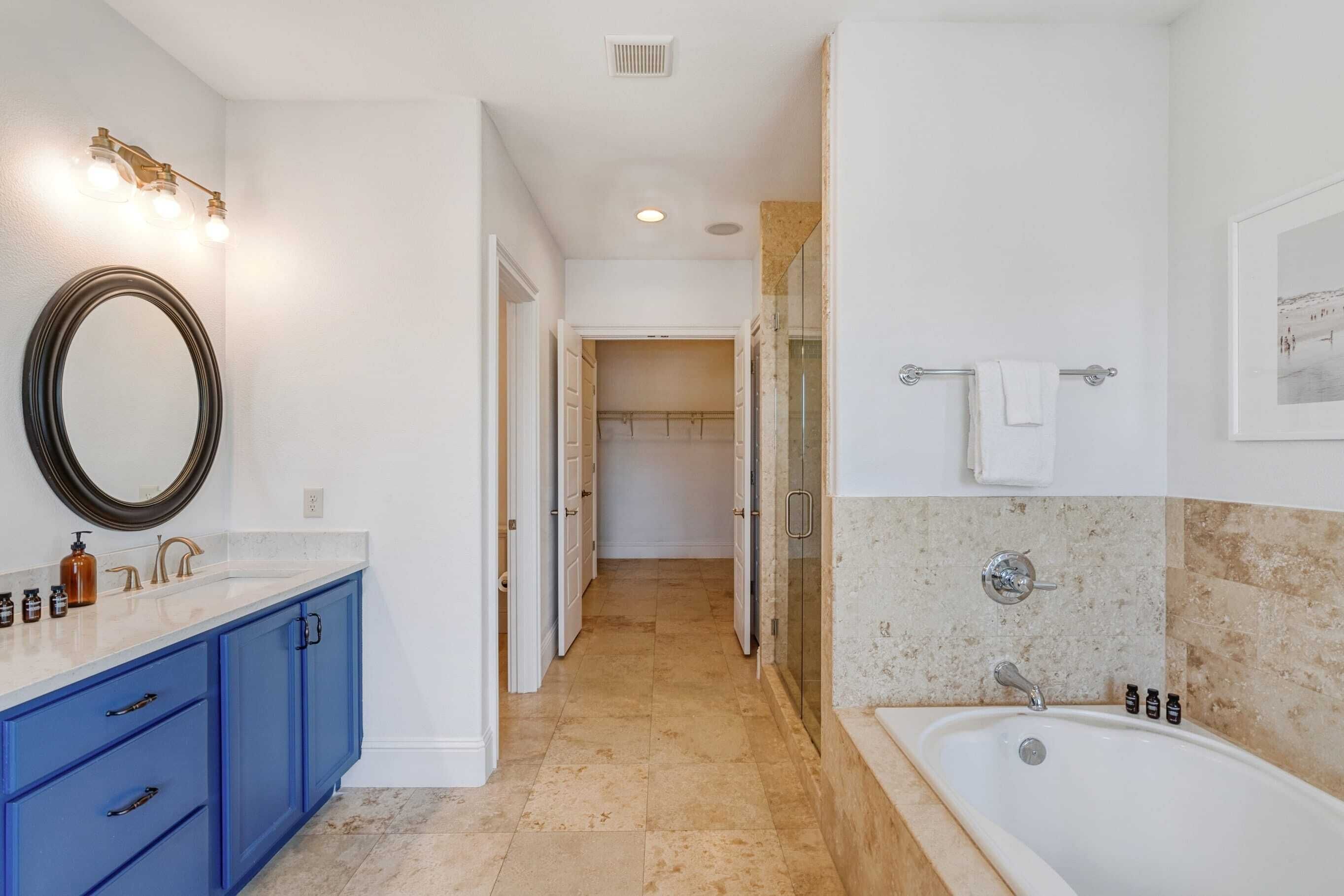 A bathroom with a bathtub, a large mirror, and a vanity with blue cabinets.