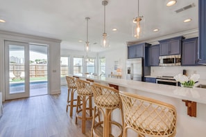 A modern kitchen with bar stools, a large island, and a view of the backyard.