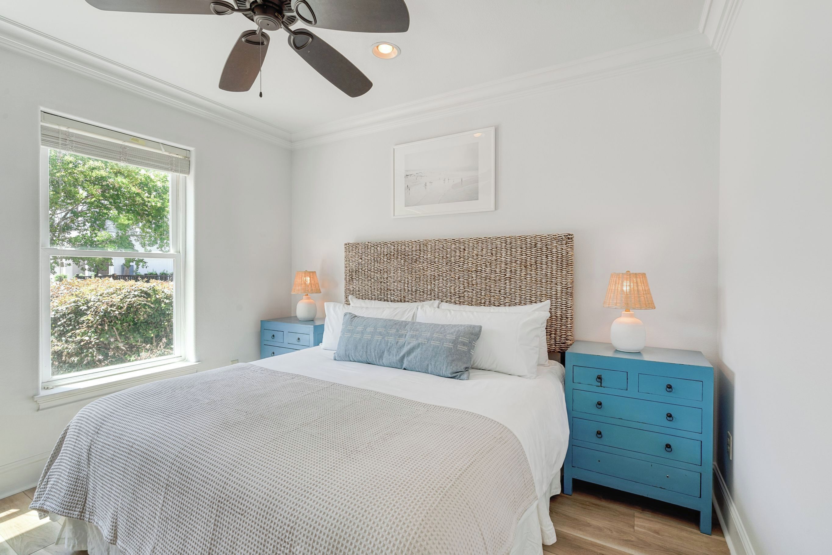 A bedroom with a bed, two nightstands, a ceiling fan, a window, and a wall-mounted picture.