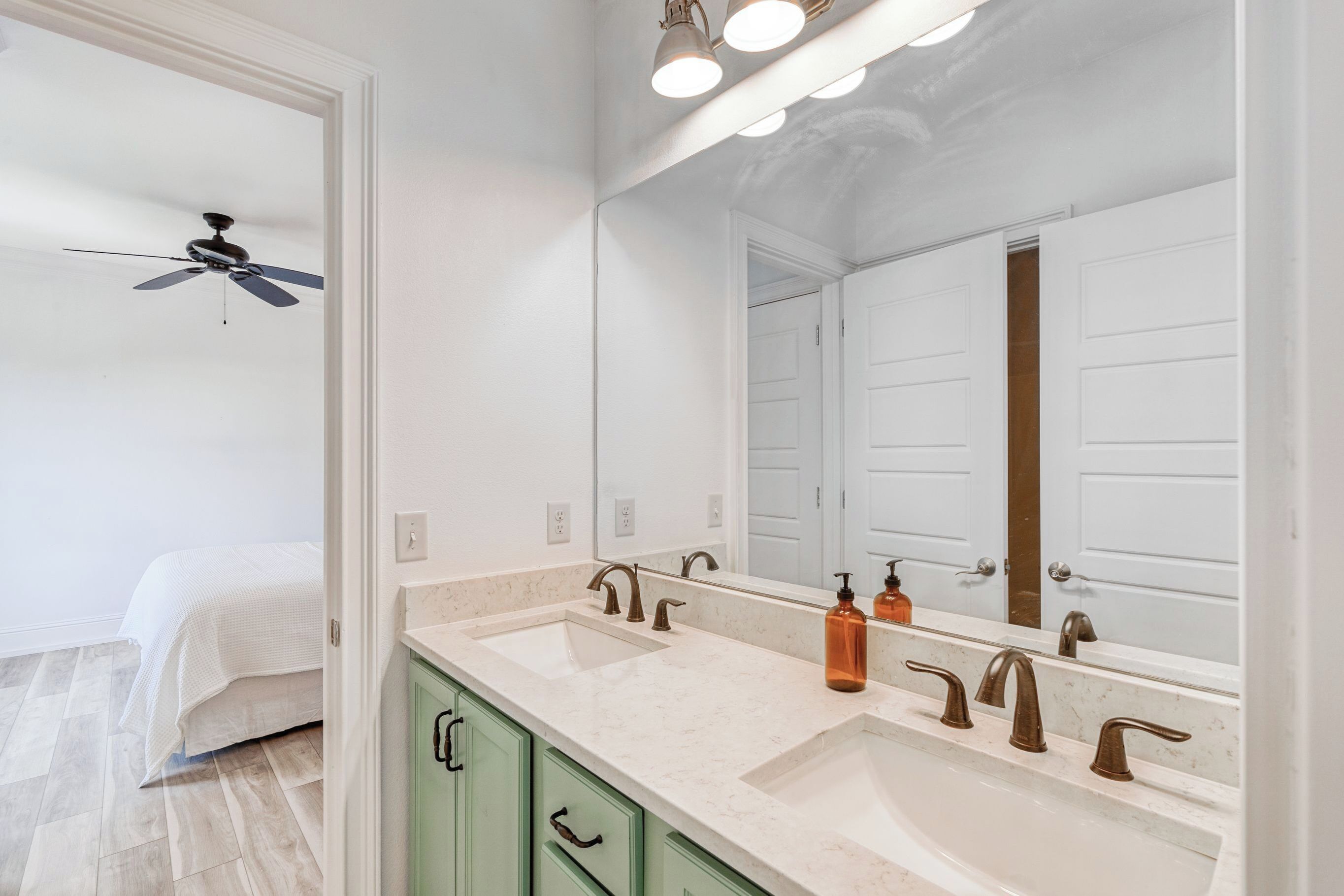 A bathroom with a double sink, a ceiling fan, and a large mirror.