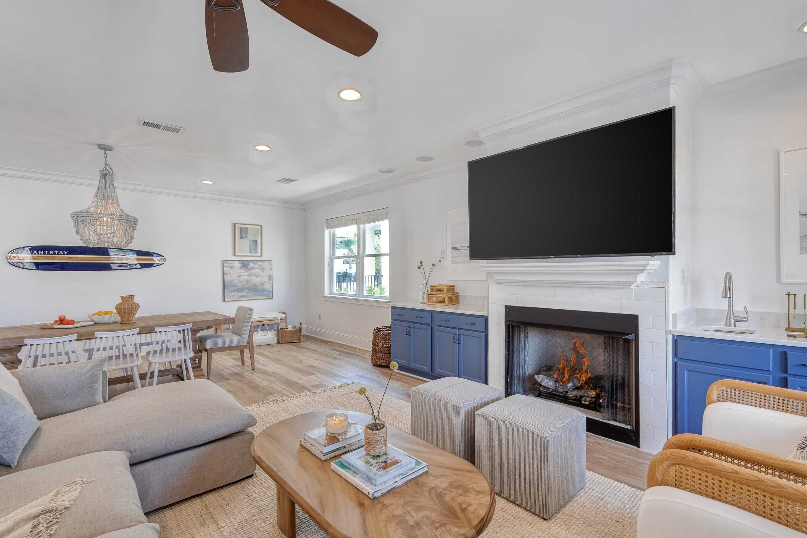 A spacious living room with a fireplace, a dining area with a table and chairs, and a large flat-screen TV mounted above the fireplace.