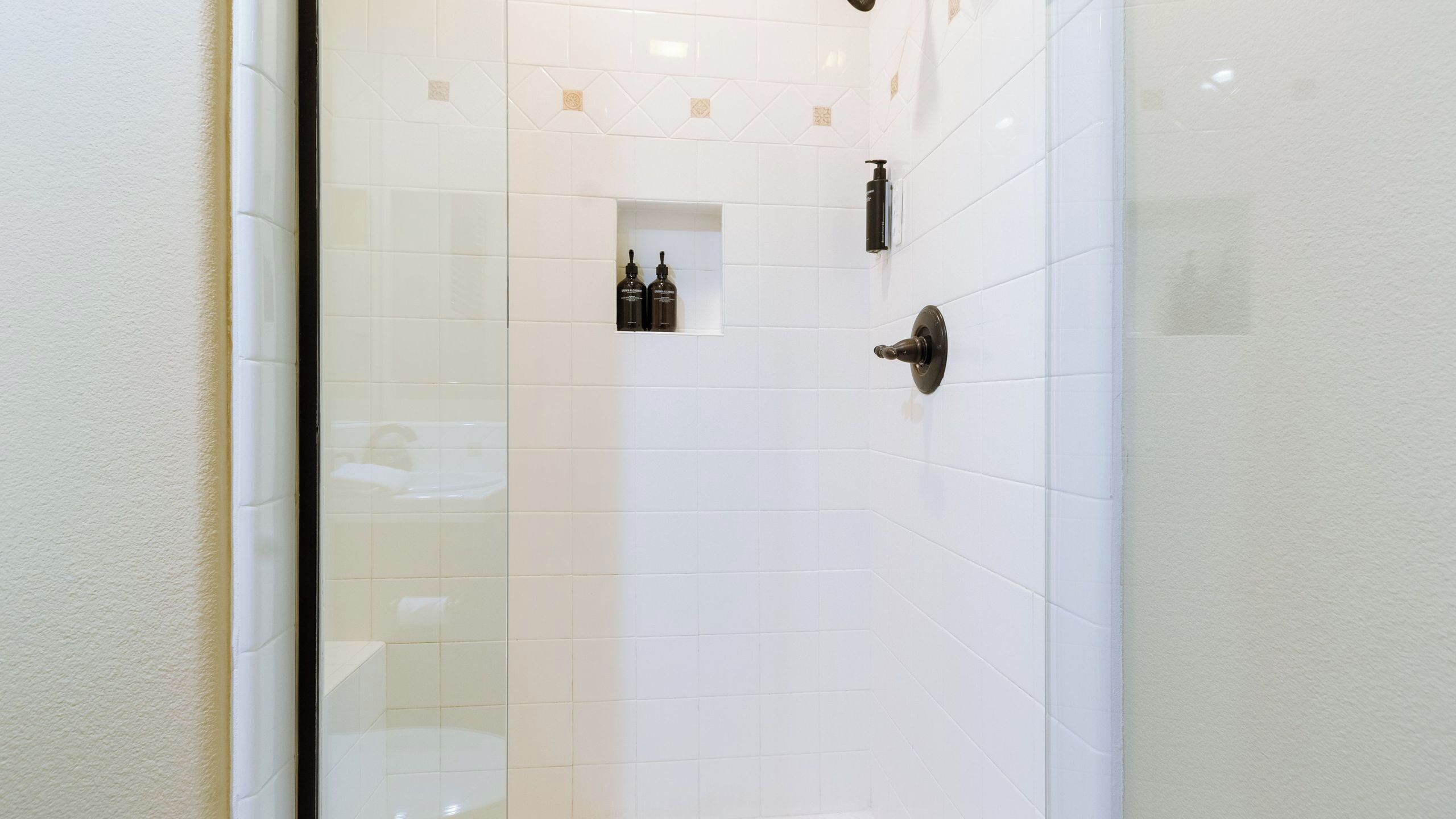 Un bagno con piastrelle bianche, una porta doccia e due flaconi appesi al muro.