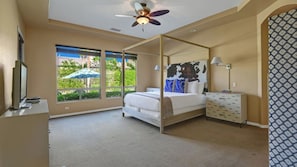 A bedroom with a four-poster bed, a ceiling fan, a large window with a view of greenery, and a patterned wall. - Songbird by Avantstay Pool, Spa & Firepit + Tons of Outdoor Seating (Indio)