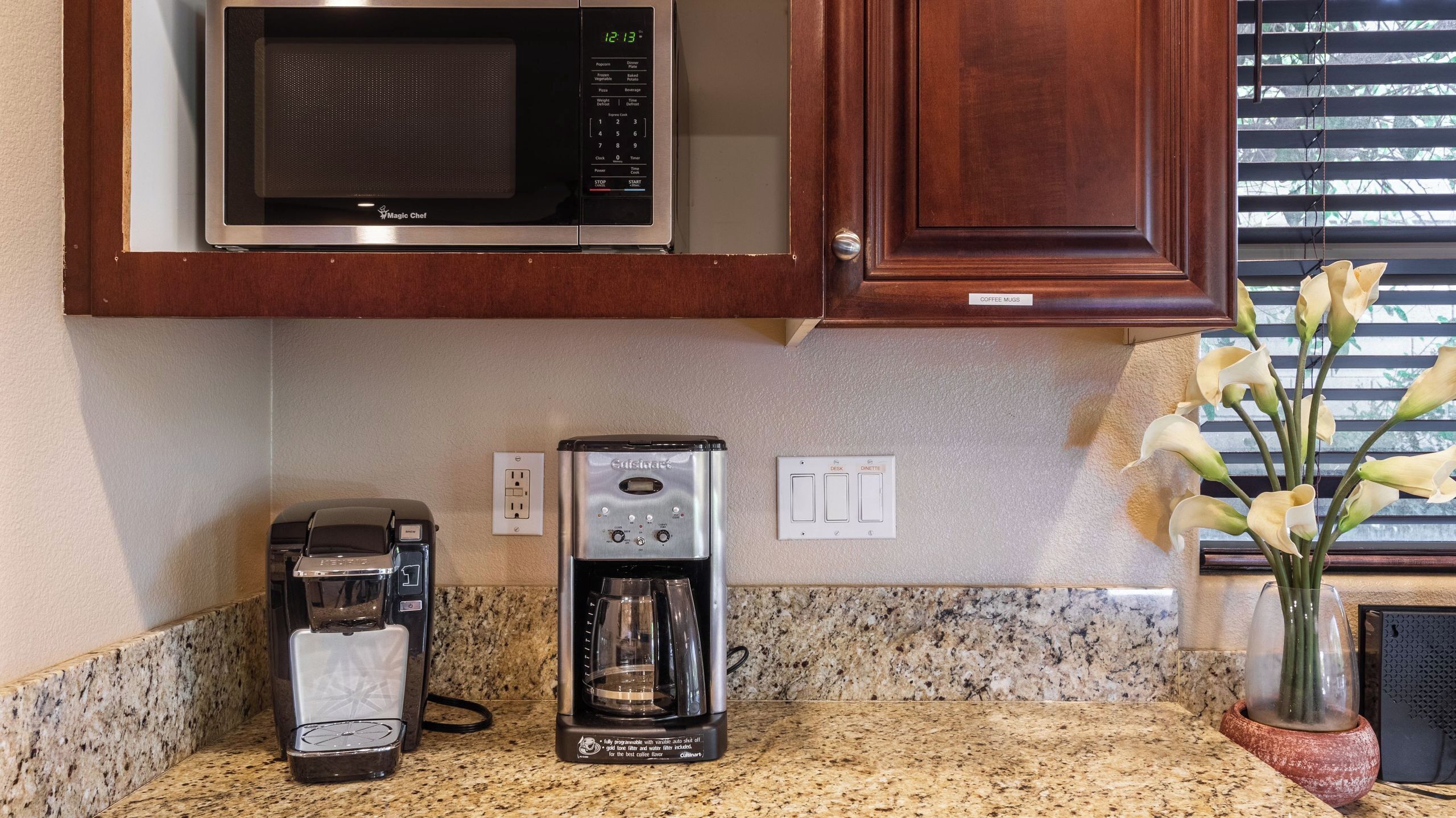 A kitchen with a microwave, coffee maker, and a coffee mug on the counter.