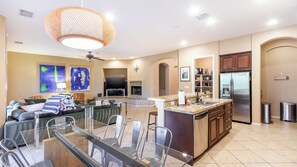 A modern kitchen with a central island, a dining area with glass-top table, and a living room with a sofa and artwork. - Songbird by Avantstay Pool, Spa & Firepit + Tons of Outdoor Seating (Indio)