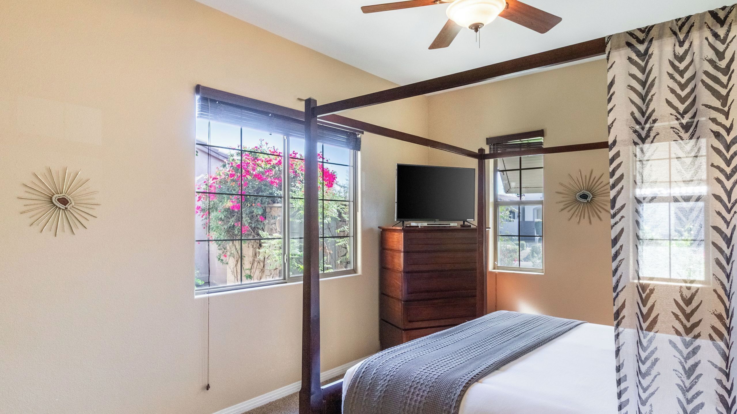 A bedroom with a bed, a dresser, a television, and a ceiling fan.