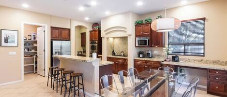 A modern kitchen with a central island, bar stools, a dining table with chairs, and built-in appliances.