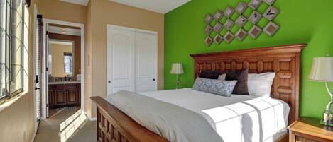 Un dormitorio con cama de madera, paredes verdes, ventilador de techo y vistas a la cocina.
