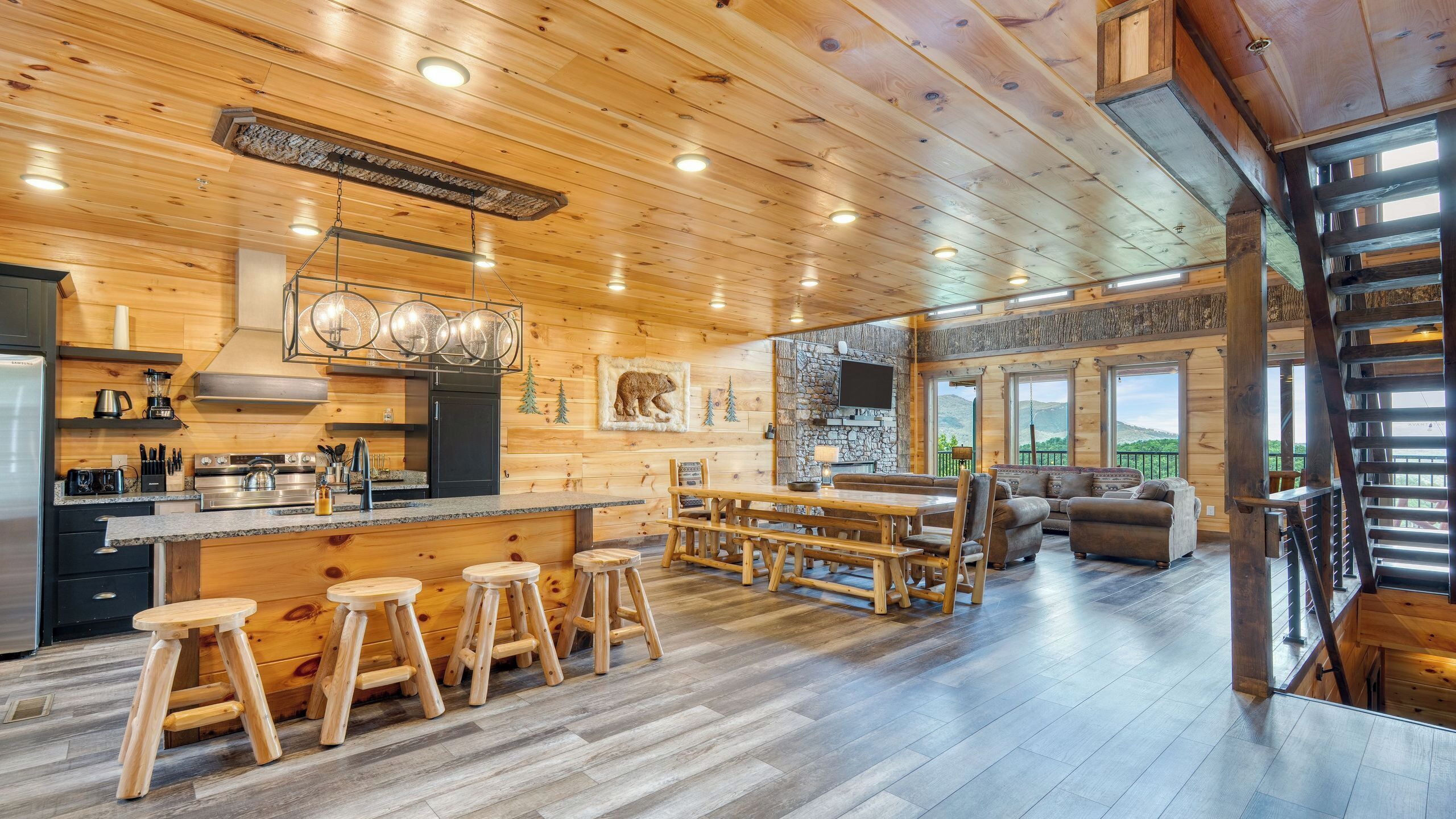 A wooden cabin interior with a kitchen, dining area, and a large window overlooking a mountainous landscape.