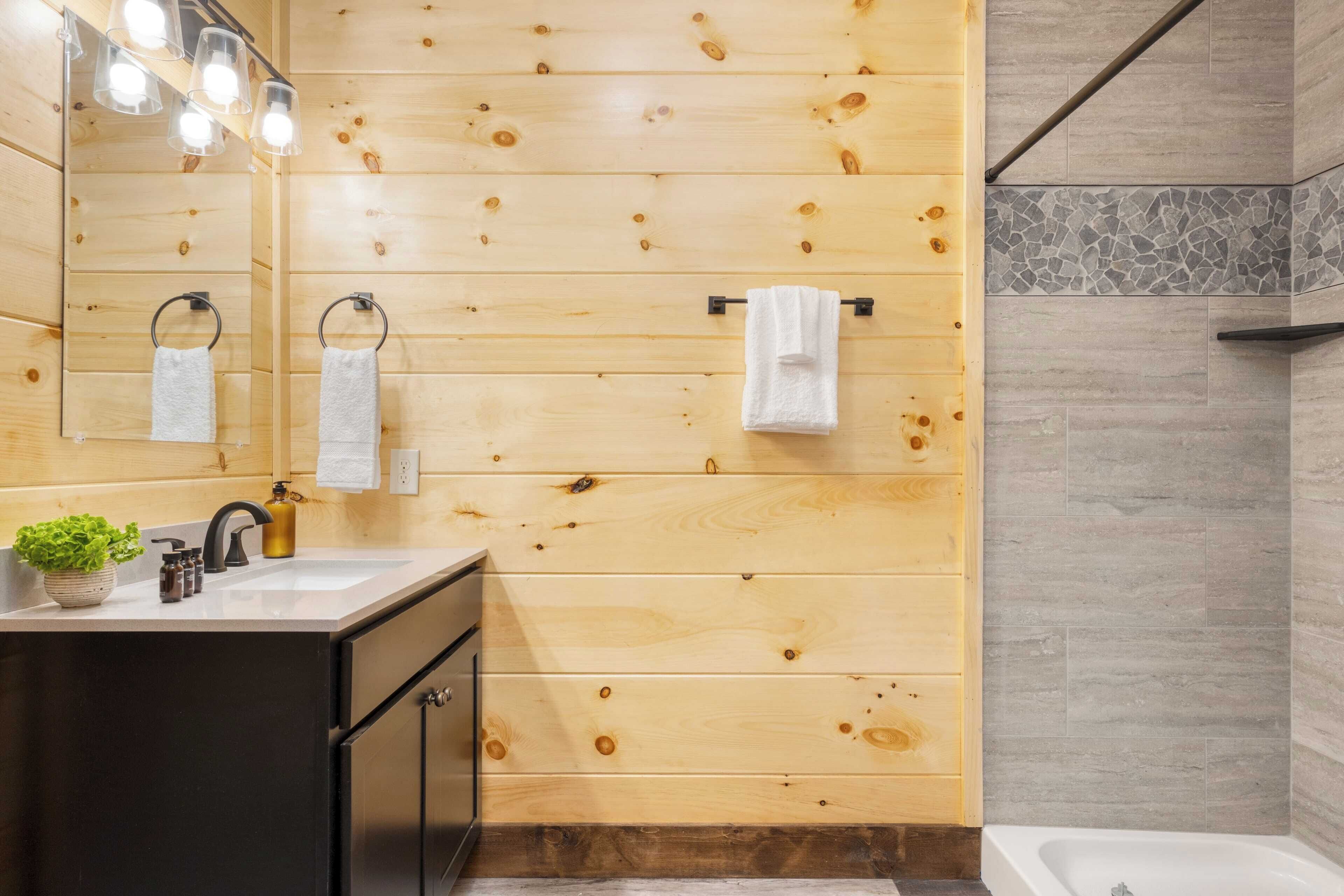 Une salle de bain aux murs lambrissés, équipée d’un lavabo, d’un miroir et d’un porte-serviettes.